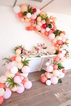 a table topped with lots of balloons and greenery next to a wall mounted balloon arch