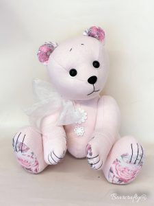 a white teddy bear with pink roses on it's chest and ears, sitting in front of a white background