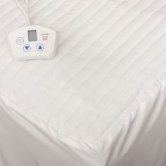 an electronic blood pressure device on top of a white bed sheet that is unmade