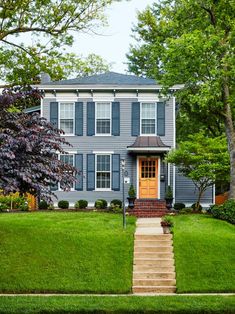 a house with stairs leading up to the front door and grass lawn in front of it