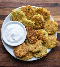 a white plate topped with fried food next to a small bowl of ranch dressing on top of a wooden table