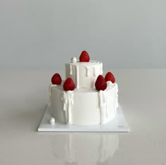 a white cake topped with strawberries on top of a table next to a wall