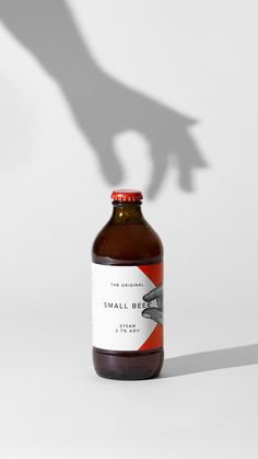 a bottle of small brown liquid sitting on top of a white table next to a person's shadow