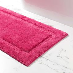 a bright pink bath mat on a marble countertop