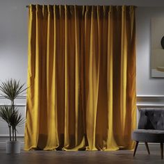 an orange curtain is hanging in front of a gray chair and potted plant on the floor