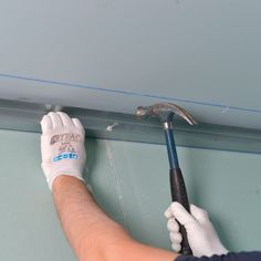 a man in white gloves holding a wrench on the side of a wall with blue paint