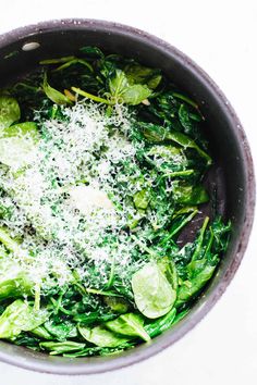 a pot filled with green vegetables covered in parmesan cheese