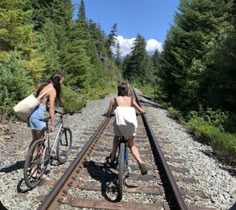 two women riding bikes on train tracks in the woods