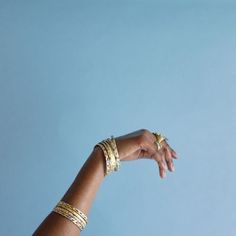 a person's hand reaching up into the sky with gold bracelets on it