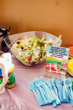 a table topped with lots of food next to a bowl of salad and plastic utensils