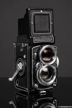 an old fashioned camera sitting on top of a black surface with its lens up to the side