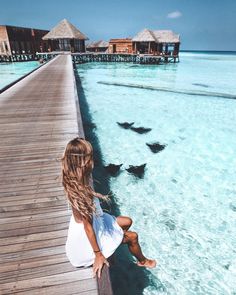 a woman sitting on a dock looking out over the water at huts in the ocean