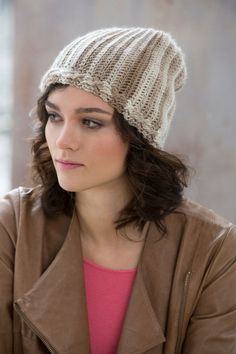 a young woman wearing a knitted hat and brown jacket looking off to the side