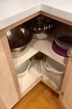 an open cabinet with bowls and pans in it