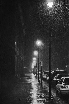 a black and white photo of cars parked on a street at night in the rain