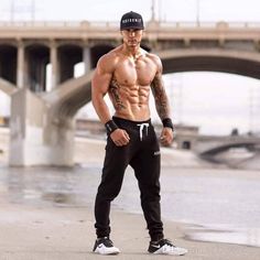 a shirtless man standing in front of a bridge with his hands on his hips