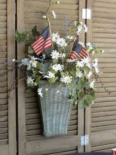 a basket with flowers and an american flag hanging on the side of a building in front of shutters