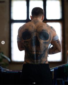 a man with tattoos on his back standing in front of a window