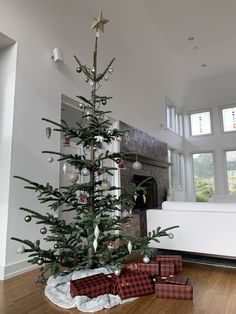 a christmas tree with presents under it on the floor in front of a fireplace and windows