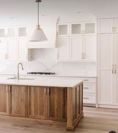 a large kitchen with white cabinets and wooden floors is pictured in this image, there are two pendant lights hanging over the island