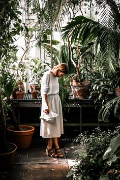 a woman in a white dress is looking at potted plants