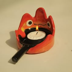 a candle holder with a red and black animal face holding a frying pan in it's mouth