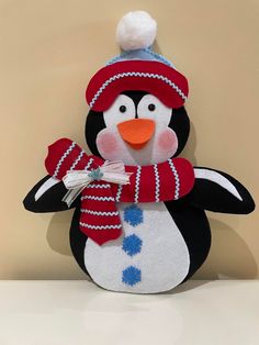 a stuffed penguin with a red hat and scarf on it's head is standing in front of a wall