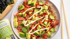 a white bowl filled with rice, avocado and sauce next to chopsticks