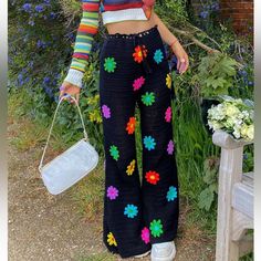 a woman standing in front of some flowers holding a white bag and wearing colorful clothing