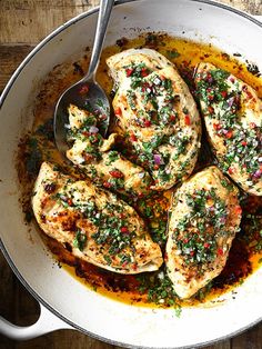 a pan filled with chicken covered in sauce and garnished with herbs