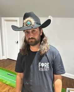 a man with long hair wearing a black hat and grey shirt in a living room