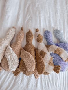 five stuffed animals lined up in a row on a white bed with the covers pulled down