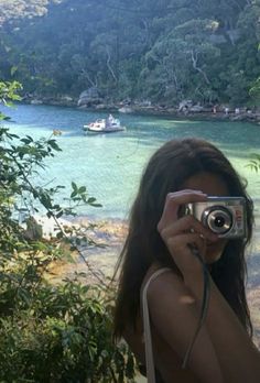 a woman taking a photo with her camera in front of a body of water and mountains