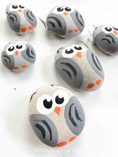 painted rocks with owls on them sitting on a white surface, one has orange eyes and the other is gray