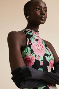 a woman in a black and pink floral print dress with gloves on her arm, looking off to the side