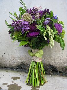 a bouquet of purple and white flowers in a vase on the ground next to a wall