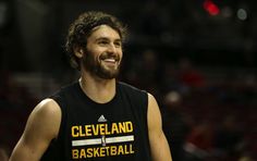 a smiling man in a cleveland basketball jersey is standing on the court with his hands behind his back