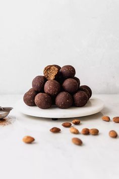 a white plate topped with chocolate covered almonds next to a pile of nuts on top of a table