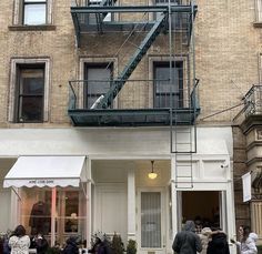 several people are walking in front of a building with a fire escape on the second floor