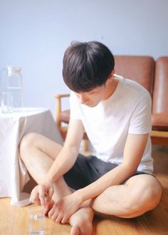 a young man sitting on the floor with his legs crossed and one hand resting on an empty glass in front of him