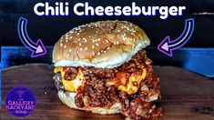 a close up of a hamburger on a wooden table with the words chilli cheeseburger above it