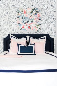 a bed with pink, blue and white pillows on it in front of a floral wallpaper