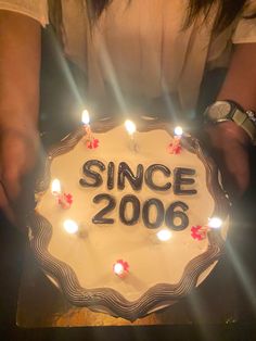 a person holding a cake with candles on it that says since 2006 in black and white