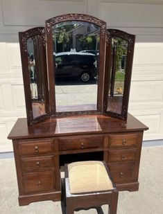 an antique vanity with mirror and stool in front of a garage door, next to a car