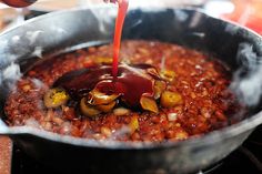 someone pouring sauce on some food in a pan