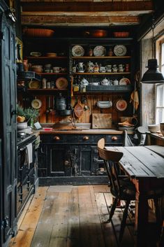 an old fashioned kitchen with wooden floors and black cabinetry, along with lots of dishes on the shelves