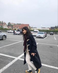 a woman walking across a parking lot next to parked cars