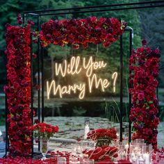 a sign that says will you marry me? surrounded by flowers and candles on a table