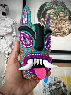 a person holding up a colorful mask with large teeth and fangs on it's face