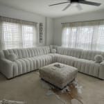 a living room filled with lots of white furniture and windows covered in blinds on top of them